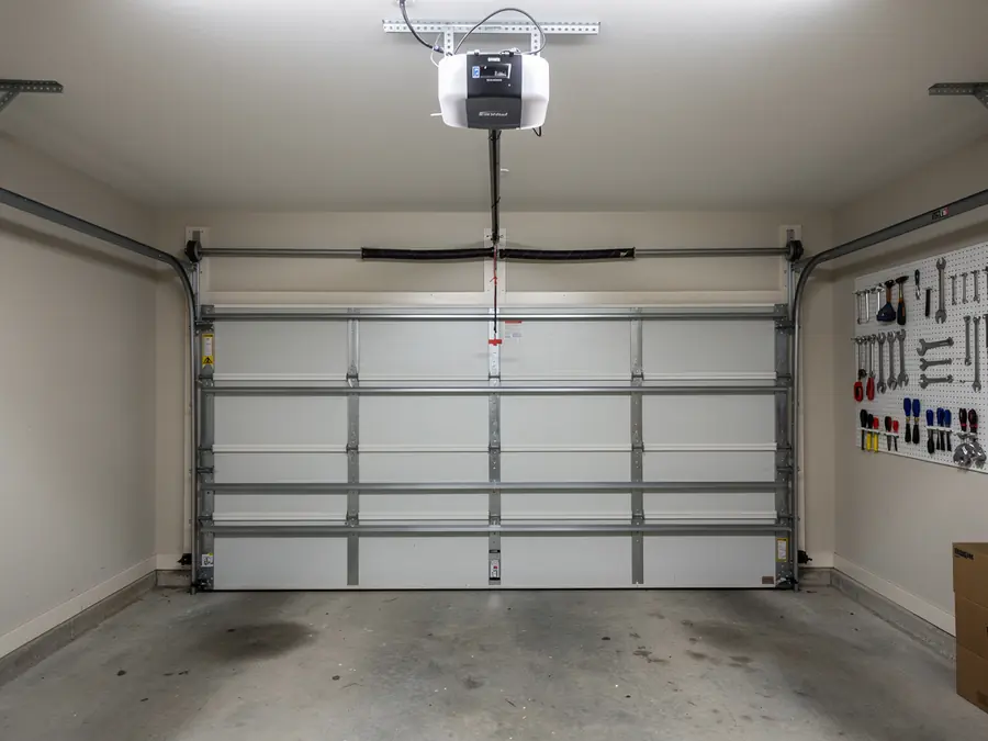 A white garage door is closed with an opener and tools on a pegboard.