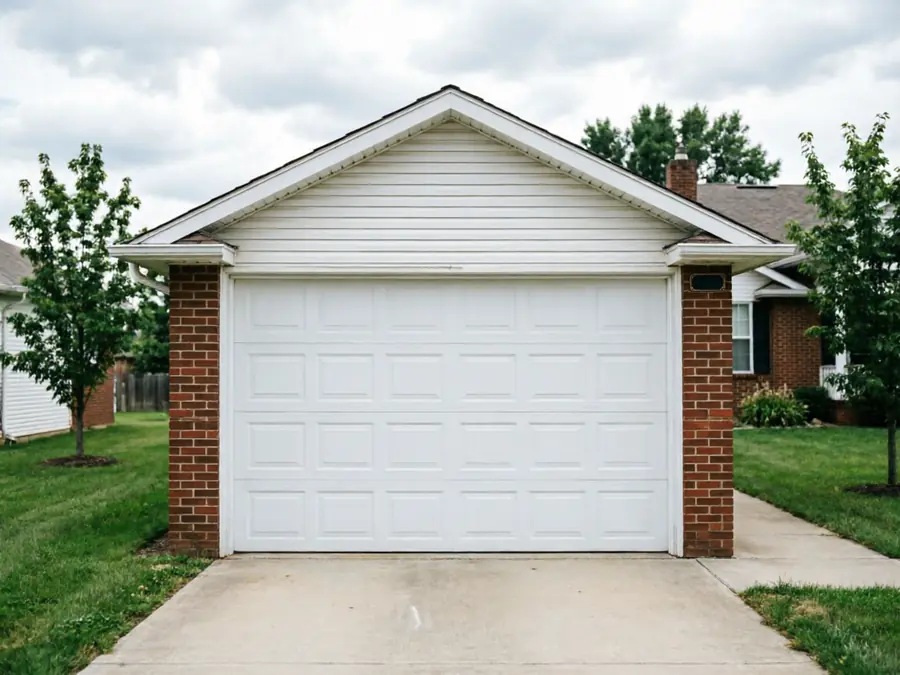 A white garage door is on a brick and siding house with a concrete driveway.